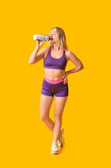 Poster - Beautiful sporty woman drinking water on yellow background. Weight loss concept