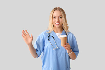 Wall Mural - Beautiful female doctor with cup of coffee waving hand on grey background