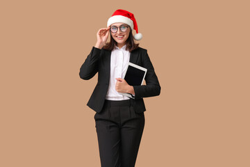 Canvas Print - Beautiful businesswoman in Santa hat with tablet on brown background