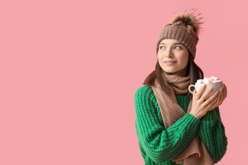 Sticker - Young woman in winter clothes with cup of hot cocoa on pink background