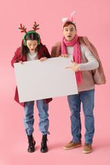 Poster - Young couple in winter clothes with blank poster on pink background