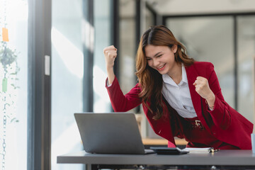 Excited cheerful business woman using laptop computer in the office, getting good news, feeling joy, laughing, making winner gesture, happy to win prize.