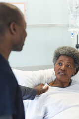 Wall Mural - African american male doctor talking with senior female patient in sunny hospital room