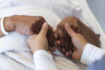 Wall Mural - Hands of diverse female doctor holding hands of senior female patient in hospital room