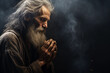 Old man praying in the dark room with his hands folded in prayer