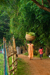 an unidentified rural woman with her son, carrying leaves over her head.