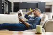 © Wavebreak Media - Happy senior biracial man lying on couch with cup of coffee and reading book at home