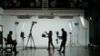 © kinomaster - Professional filming pavilion with a white cyclorama. Shooting of a girl in a red dress who sings into a retro microphone. Director, Cameraman and crew in Backstage.