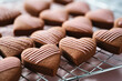 Close-up of chocolate heart cookies with chocolate drizzle on a cooling rack. Delicious shortbread cookies with icing, baking for valentines day, romantic dessert.
