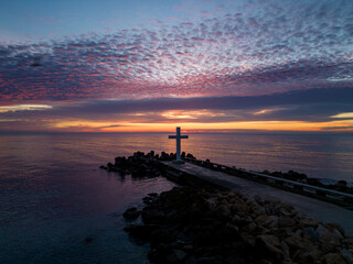 Wall Mural - A flight around a Christian Holy cross early in the morning at sunrise. The large cross stands on the edge of a breakwater on the sea coast