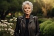 © CogniLens - Portrait of a glad woman in her 70s sporting a classic leather jacket against a lush green garden. AI Generation