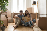 Fototapeta  - Young family with child sit on floor at new flat near boxes with stuff use tablet, browse internet, discuss furniture purchase. Spouses buy items for new house on relocation. Move-in day, e-commerce