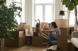 © fizkes - Cheerful cute child jump out from box happy about moving to new home, family play in living room near heap of stuff. Young parents spend time together celebrate relocation day. Real estate, ownership