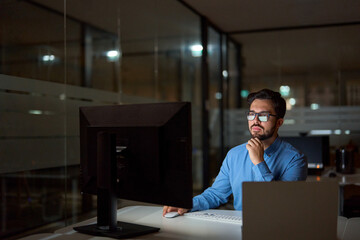 Busy business man software developer using computer working late in office. Professional businessman looking at pc typing searching online solution at night sitting at workplace desk in dark office.