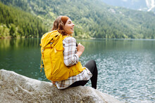 Young Woman Traveler With A Bright Hiking Backpack On A High-mountain Lake. The Image Of Travelers. Adventure, Vacation Concept. Active Lifestyle.