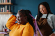 © gstockstudio - Happy African hairdresser braiding hair to a smiling female customer in salon