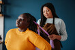 © gstockstudio - Confident African hairdresser braiding hair to a smiling female customer in salon