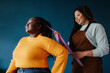 © gstockstudio - Happy African American hairdresser braiding hair to a female customer on blue background
