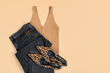 Black jeans, tank top and leopard print shoes on beige background. Fashion spring, summer or autumn outfit. Women's stylish and elegant clothes with accessory.  Flat lay, top view, overhead.