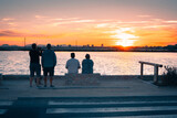 Fototapeta  - Personas junto al  mar contemplando el atardecer cuando el Sol esta apunto de perderse en el horizonte