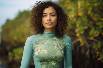 Wall Mural - Portrait of a satisfied woman in her 20s showing off a vibrant rash guard against a soft green background. AI Generation