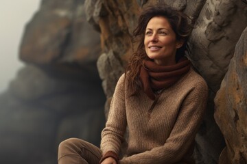 Wall Mural - Portrait of a cheerful woman in her 40s dressed in a warm wool sweater against a rocky cliff background. AI Generation