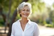 © CogniLens - Portrait of a satisfied woman in her 60s wearing a classic white shirt against a bright and cheerful park background. AI Generation