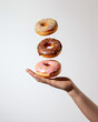 Hand Holding a Delicious Donut, tree doughnut topped with chocolate, pink glazed sweets and multi-colored sprinkle, creative and funny photoshoot for donut brand 