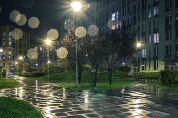 Night park paths and colored houses on a rainy autumn night. Night paths, benches, lanterns in a beautiful residential complex. Night autumn park with lanterns, benches, yellow leaves. Kyiv. Ukraine