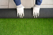 Men's hands holding a roll of artificial grass and installing it on a house. Artificial grass background.