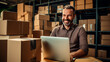 hombre adulto sonriente trabajando en una laptop en un almacén lleno de cajas 