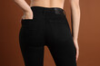 © New Africa - Woman wearing stylish black jeans on brown background, closeup
