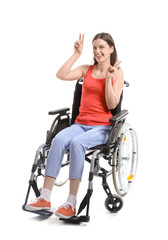 Wall Mural - Young woman in wheelchair showing victory gesture on white background