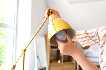 Wall Mural - Woman changing light bulb in desk lamp at home, closeup