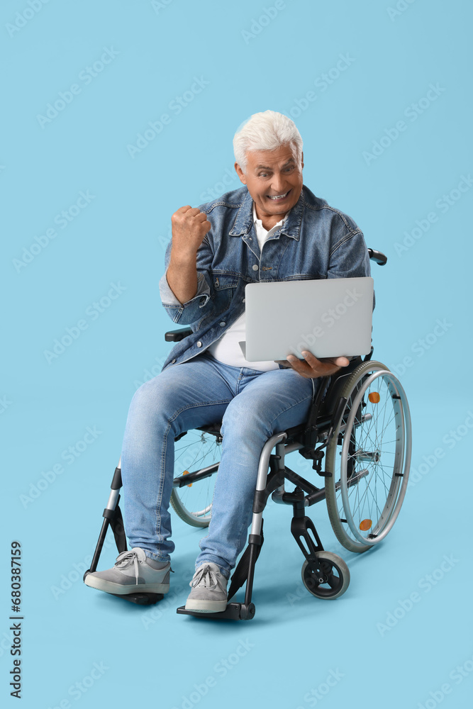 Mature man in wheelchair with laptop on blue background