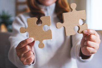 Wall Mural - Closeup image of a woman holding and putting a piece of wooden jigsaw puzzle together