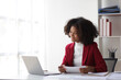 © Kainnika - Attractive african american businesswoman working with laptop and financial documents on office desk.