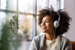 Joyful woman listening music with a headphones at the window, relaxing at home.