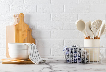 A set of kitchen utensils on a light stone countertop against a white brick wall. Kitchen textiles. A cosy kitchen with no waste. Front view.