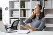 © Kainnika - A woman is using a smartphone in a library office to send text messages and listen to music when wearing headphones.
