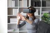 Fototapeta Sypialnia - A woman sitting on a sofa in the living room wearing VR 3D glasses looks excited about a movie.