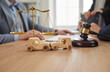 Close up photo of small wooden toy cars in front of judge's gavel and scales and the lawyer working at the desk in office with client on background. Car accident, legal law and auto insurance concept