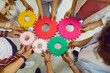 © Studio Romantic - Young people hands connect multy colored cogwheels to make gear. Symbol of collaboration, teamwork, team building, connection, partnership and integration. Business cooperation concept.
