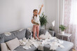 © Aleksandr - Little girl jumps on the sofa and scatters napkins. Kid make a mess at home. Chaos at home