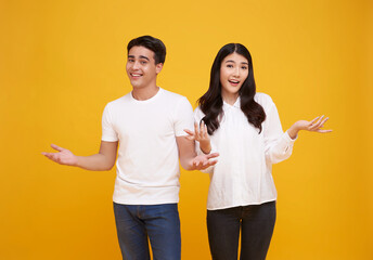 Wall Mural - Portrait of happy cheerful awesome Asian couple with big smiles opening hands on isolated yellow background.