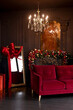 © sergiophoto - Interior of luxury dark living room with fireplace, comfortable sofa and chandelier decorated with Christmas tree and gifts in red color