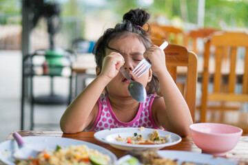 Wall Mural - Asian child cute or kid girl has anorexia or sad and bored food or boredom with frown on wood table for breakfast or lunch eating at restaurant on preschool or nursery