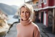 © CogniLens - Portrait of a glad woman in her 50s wearing a classic turtleneck sweater against a picturesque seaside village. AI Generation