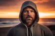 © CogniLens - Portrait of a content man in his 40s sporting a comfortable hoodie against a stunning sunset beach background. AI Generation