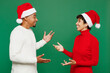 © ViDi Studio - Merry fun young couple friends man woman wear red casual clothes Santa hat posing look to each other talk speak meet isolated on plain green background. Happy New Year 2024 Christmas holiday concept.